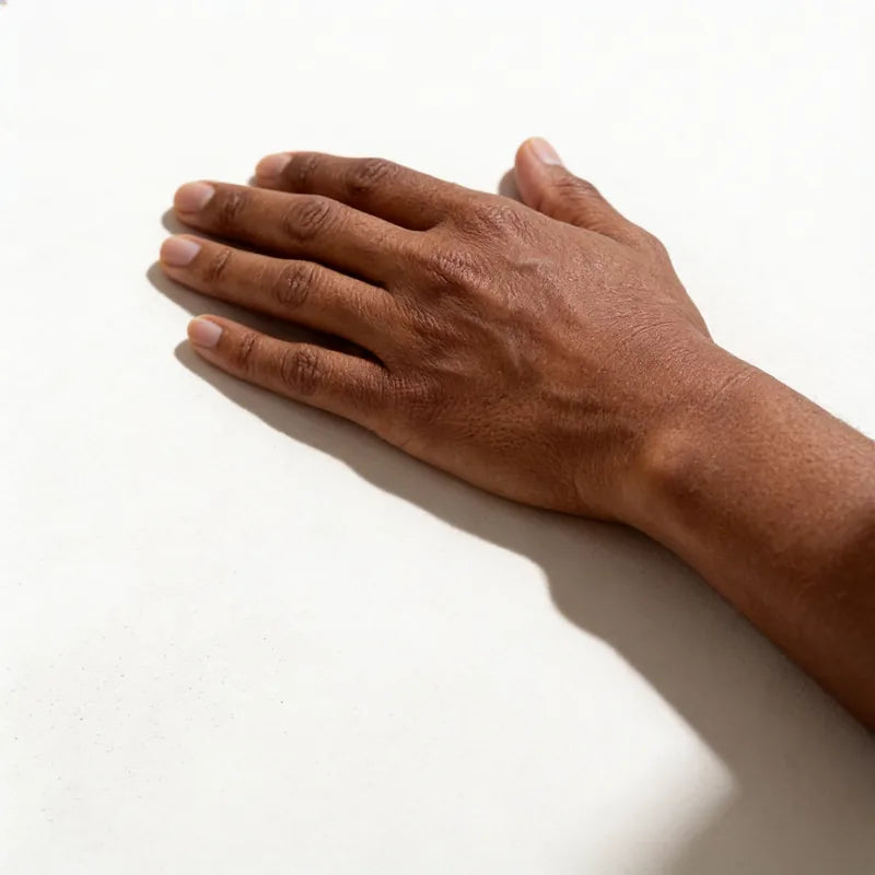 The back of a relaxed hand with deep brown skin resting on a warm off-white surface.