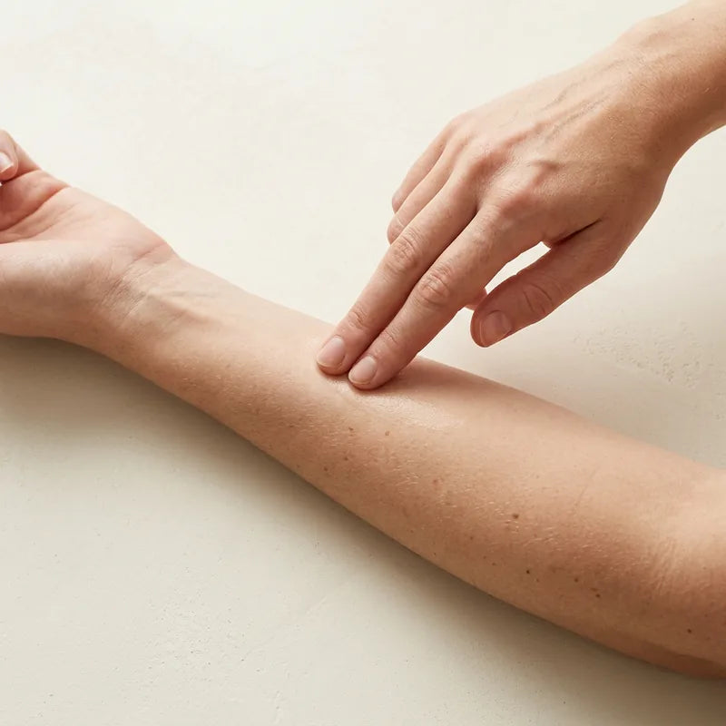 Two fingers pressing the serum into the skin of a forearm.